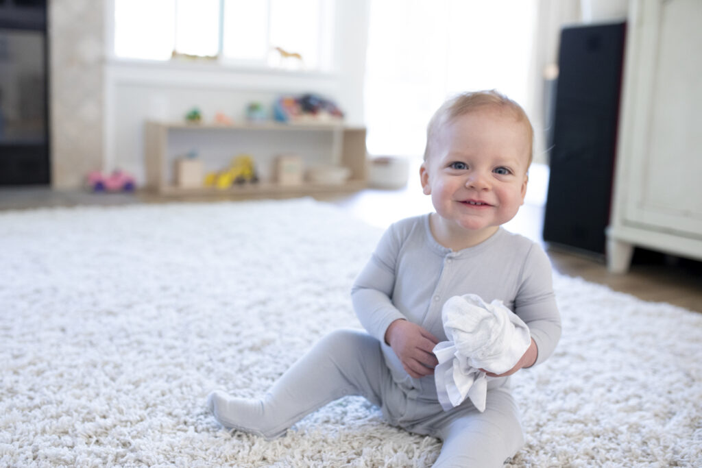 Toddler sitting on the floor in his home smiling at the camera