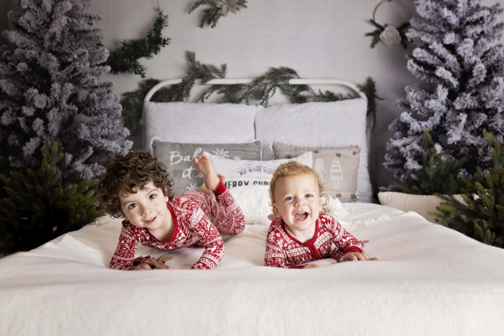 two boys in Christmas pajamas playing on a bed with a Christmas theme