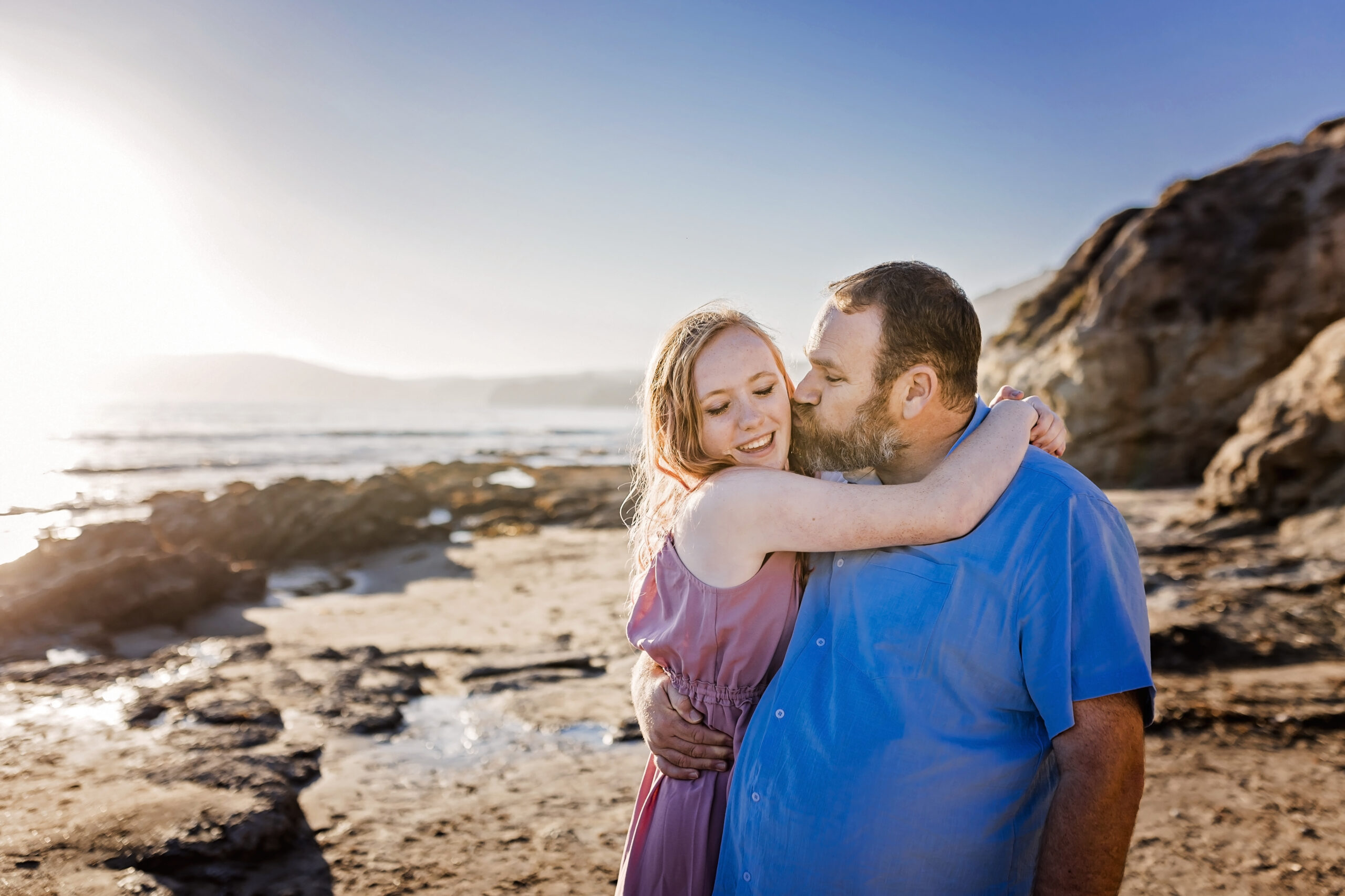 father and teenage daughter embrace on the beach