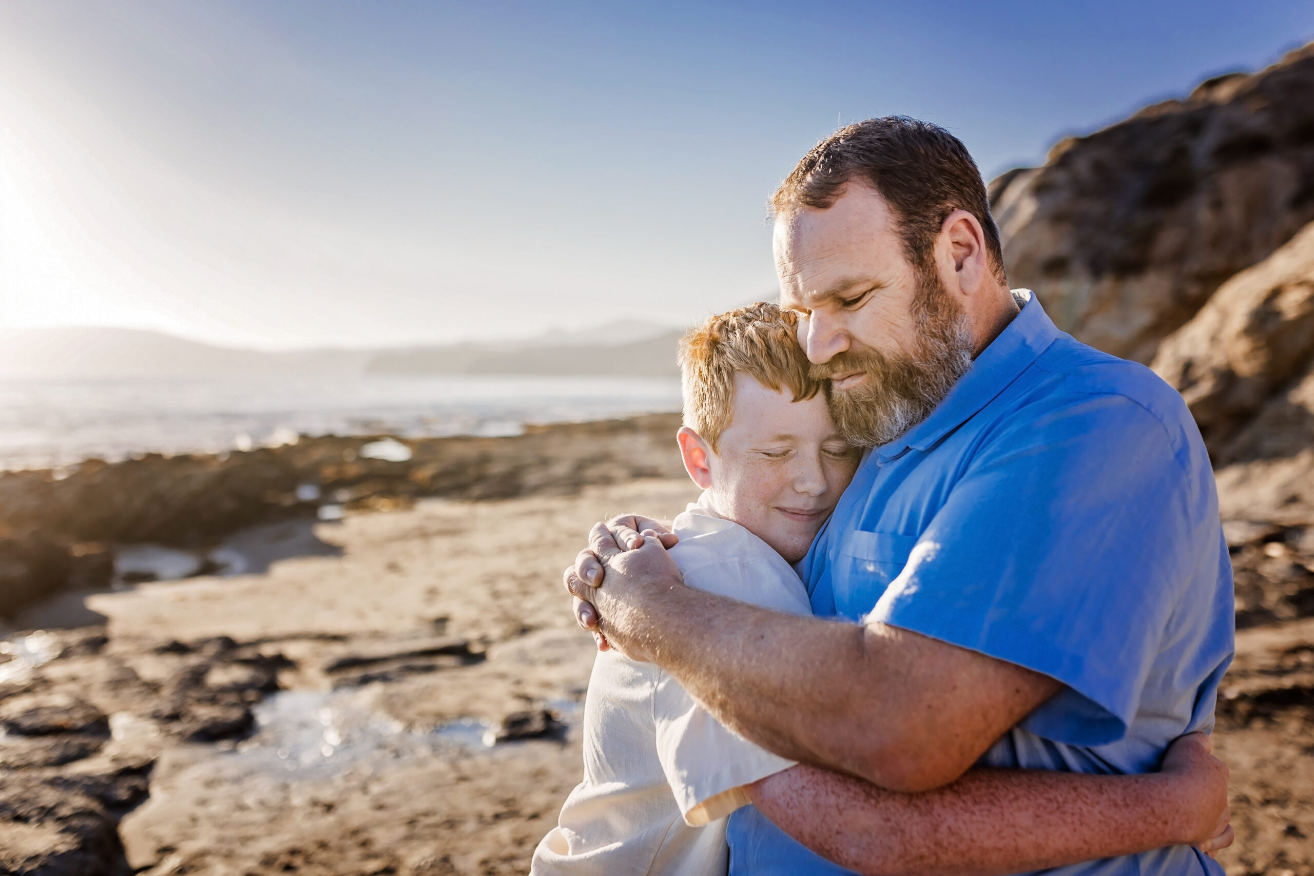 father and teenage son embrace on the beach
