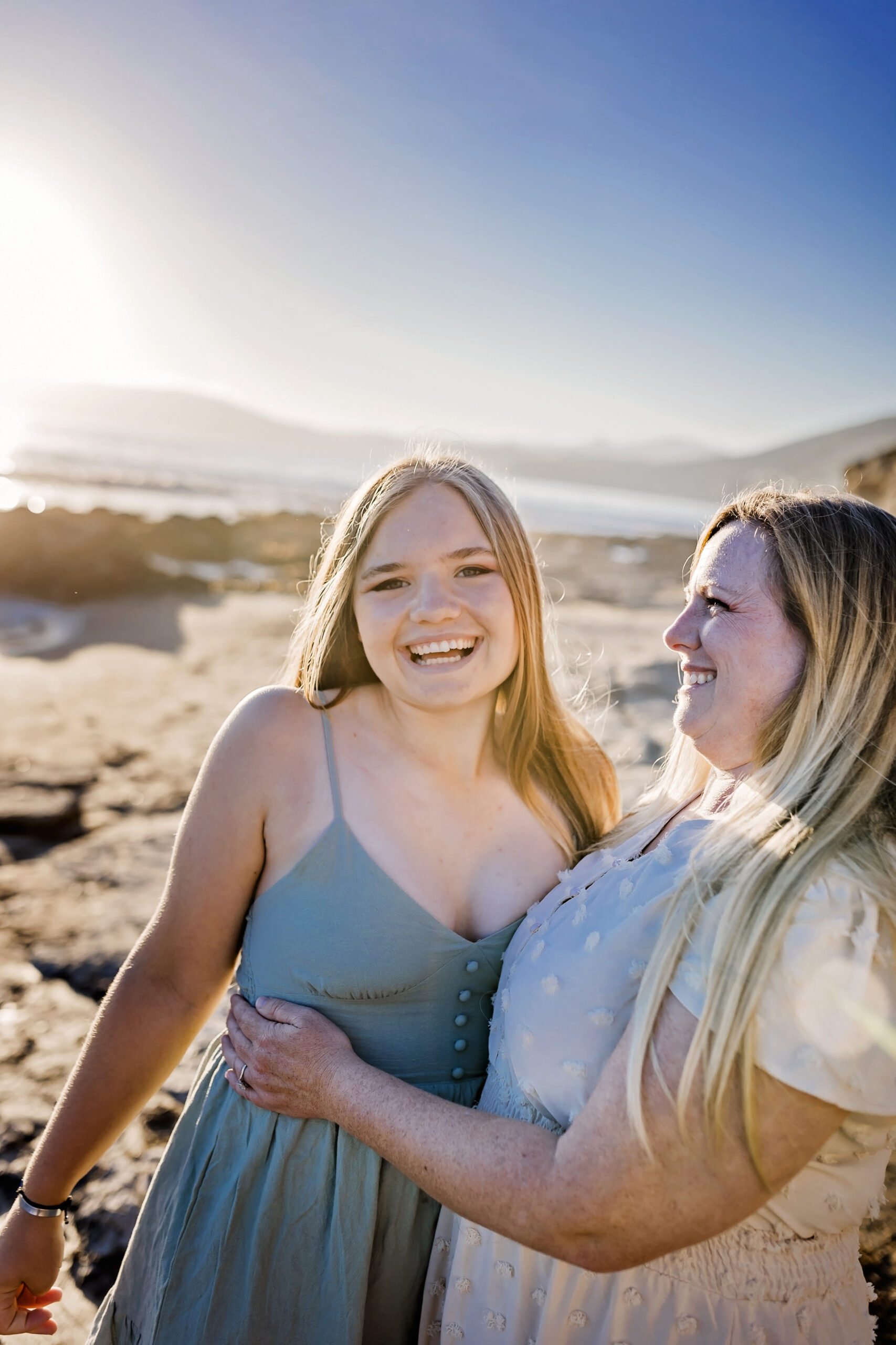 mother and teenage daughter laugh together on the beach
