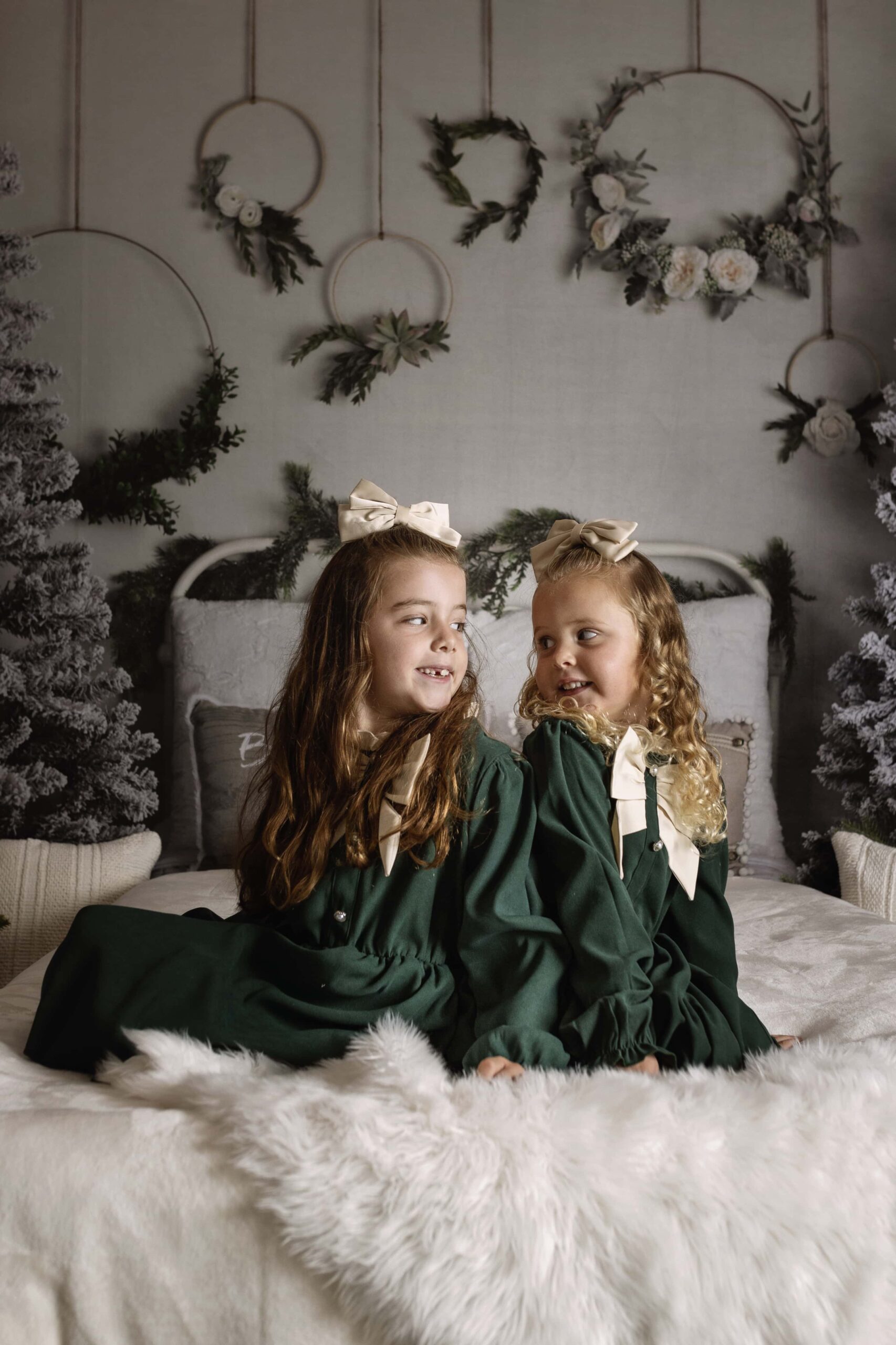 two girls in green dresses sitting on a bed in a Christmas themed studio set