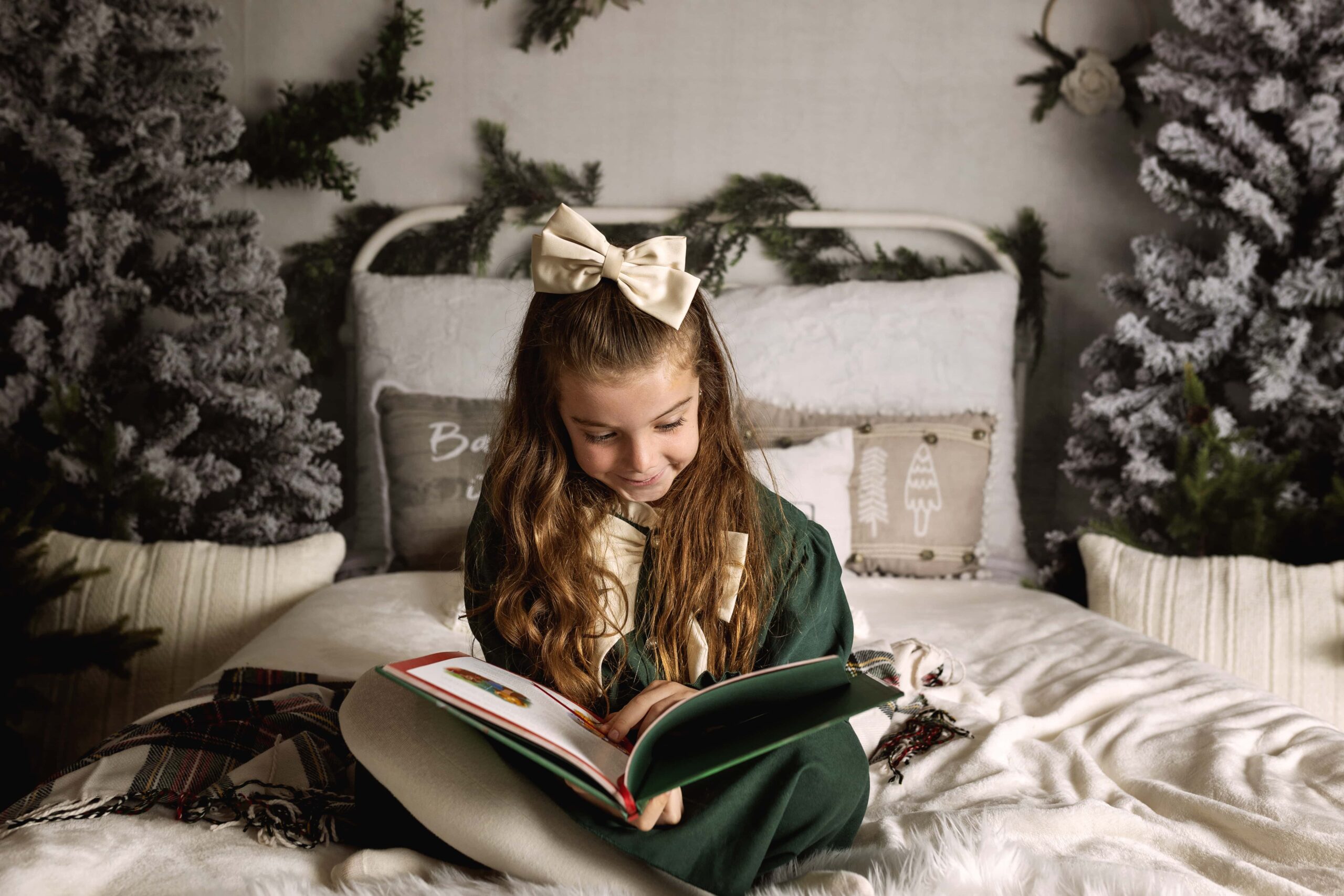 Young girl in a green dress reading a book in a Christmas themed bed set