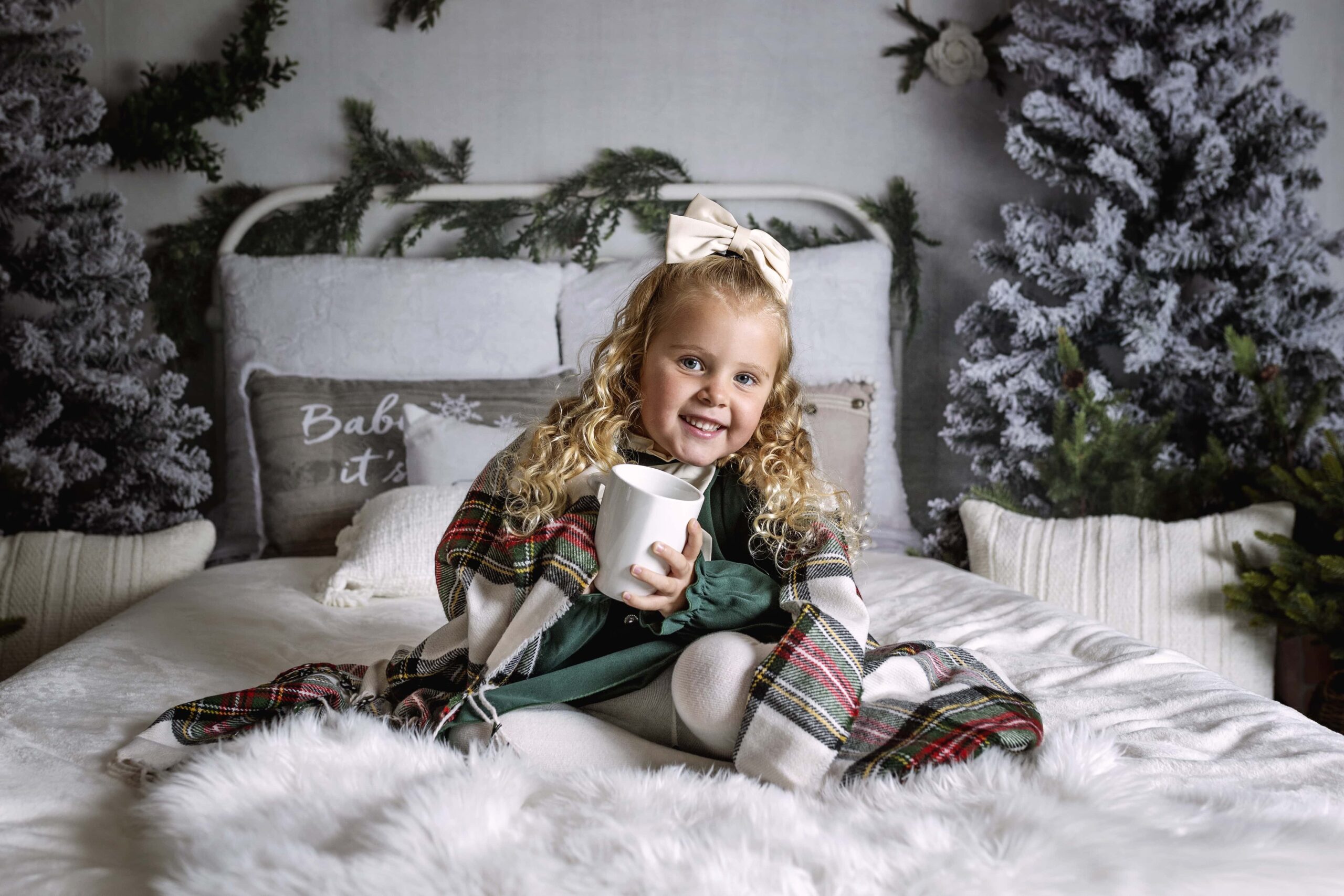 Young girl sitting on a Christmas themed bed holding a cup of hot chocolate