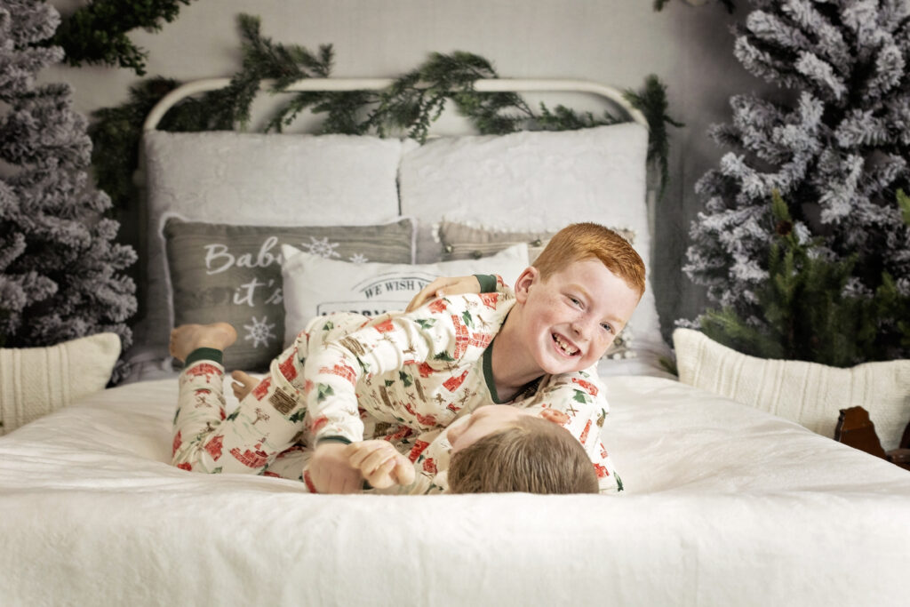 two boys in Christmas pajamas wrestling on a bed