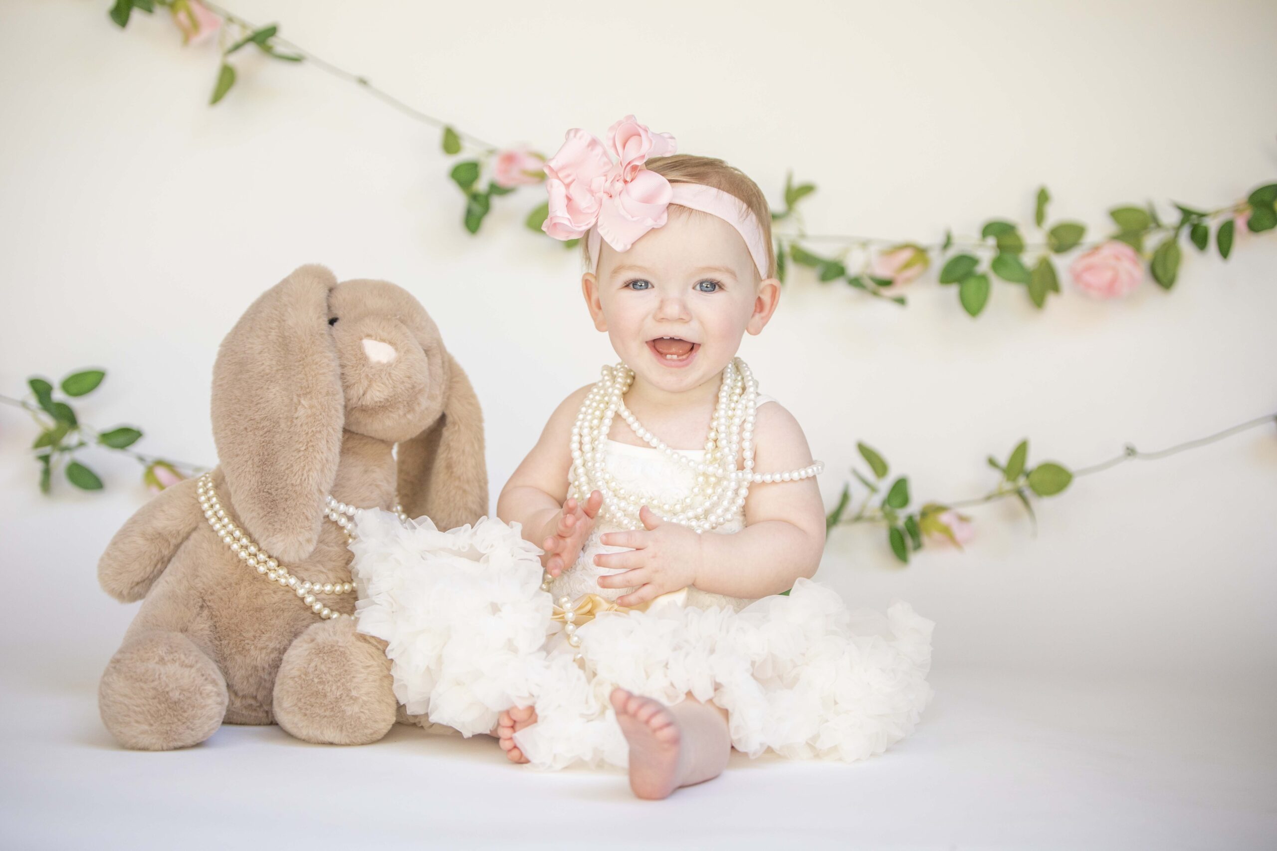 One year old girl sitting with her bunny in front of a floral garland