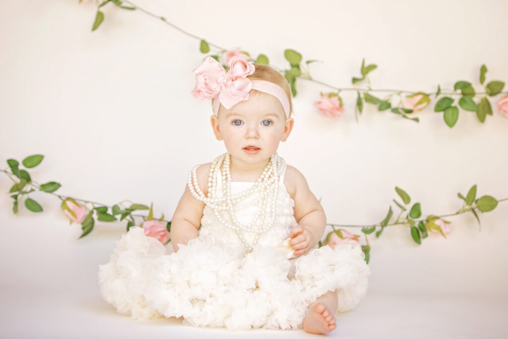One year old girl in front of gold balloons and a floral garland