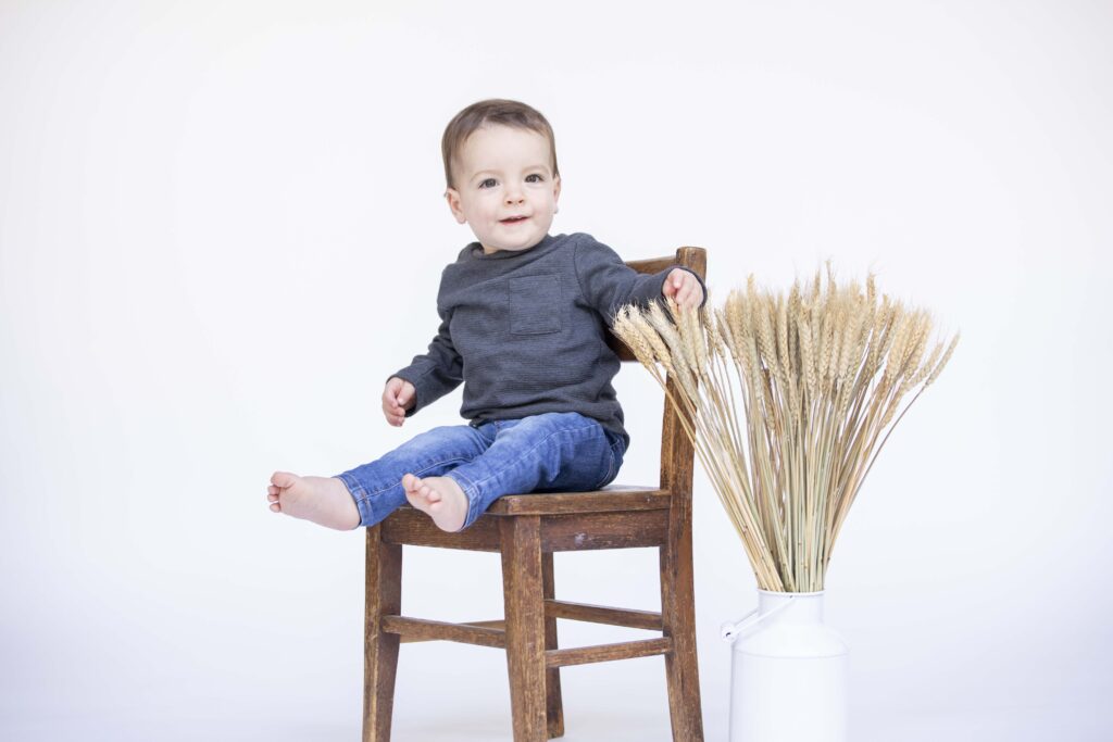one year old boy playing with wheat stalks while sitting in a chair