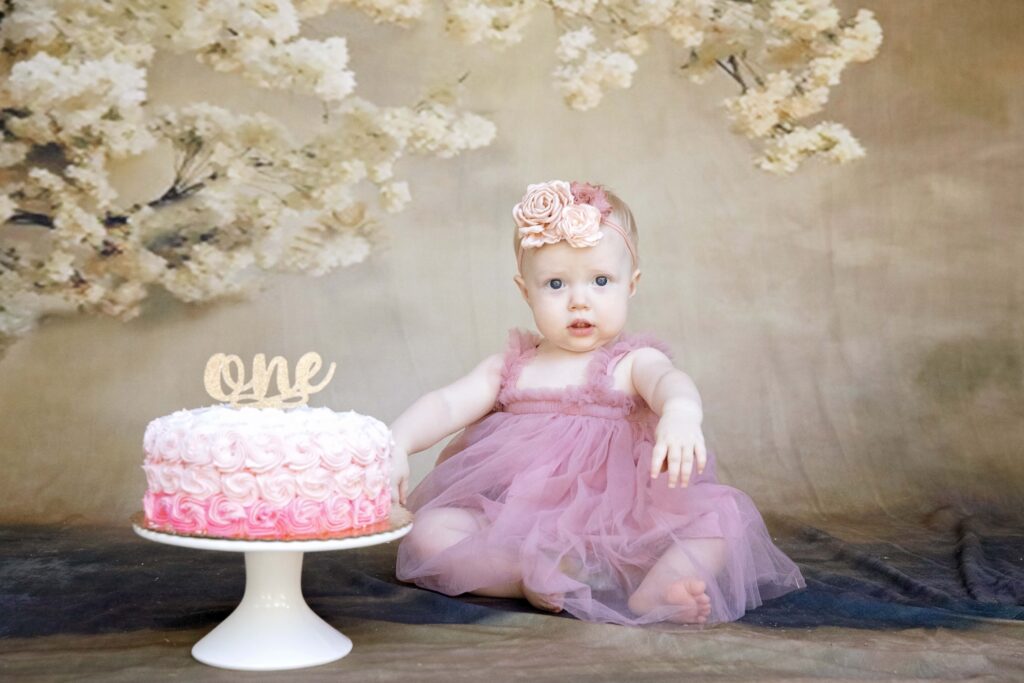 one year old girl sitting with her pink birthday cake