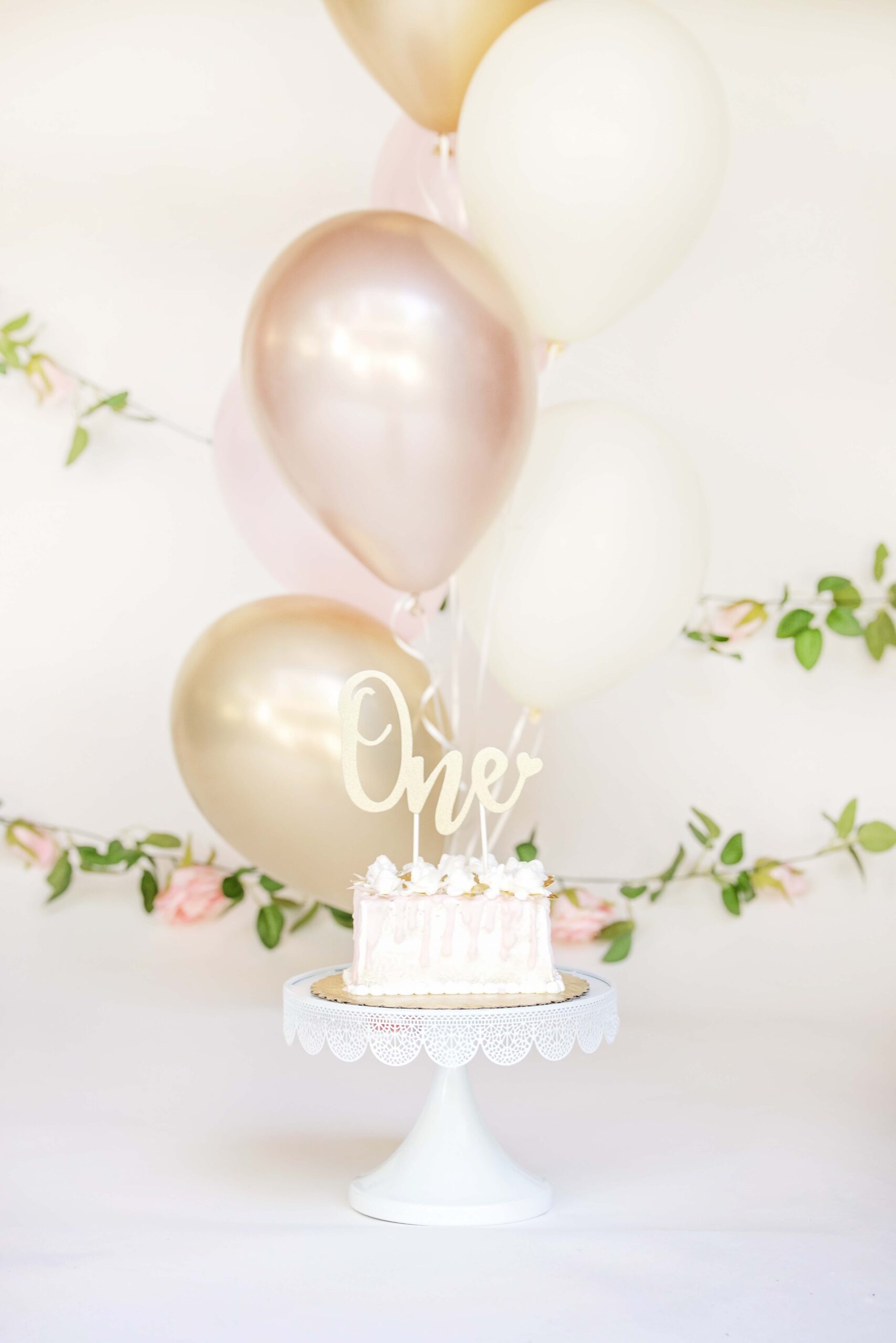 Cake for a cake smash in front of gold balloons and a floral garland