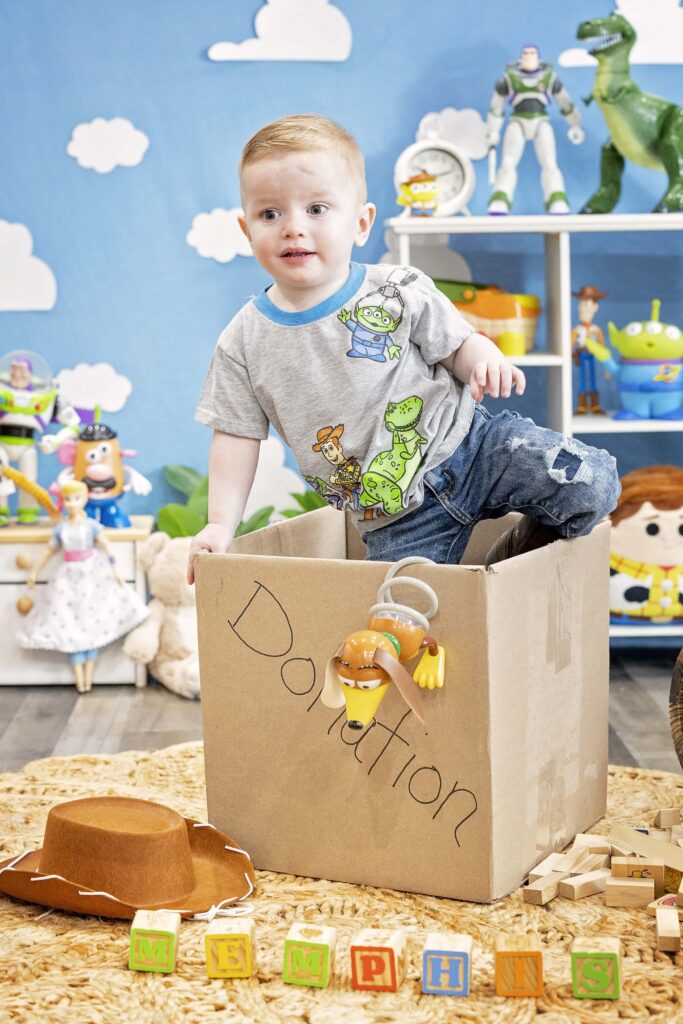 Two year old boy climbing out of a box with Toy Story items around him