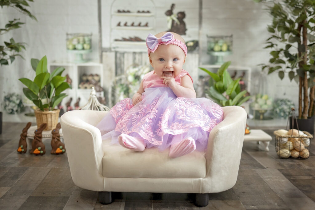 5 month old girl sitting on a mini sofa wearing a pink easter dress