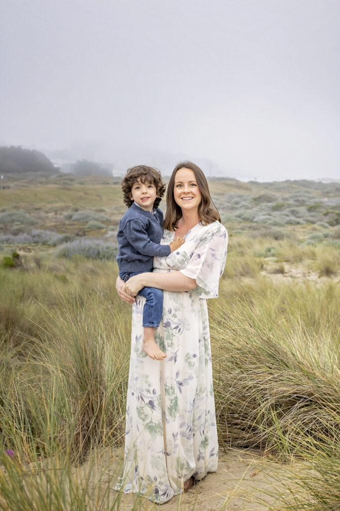 mother holding her young son while standing among patches of beach grass