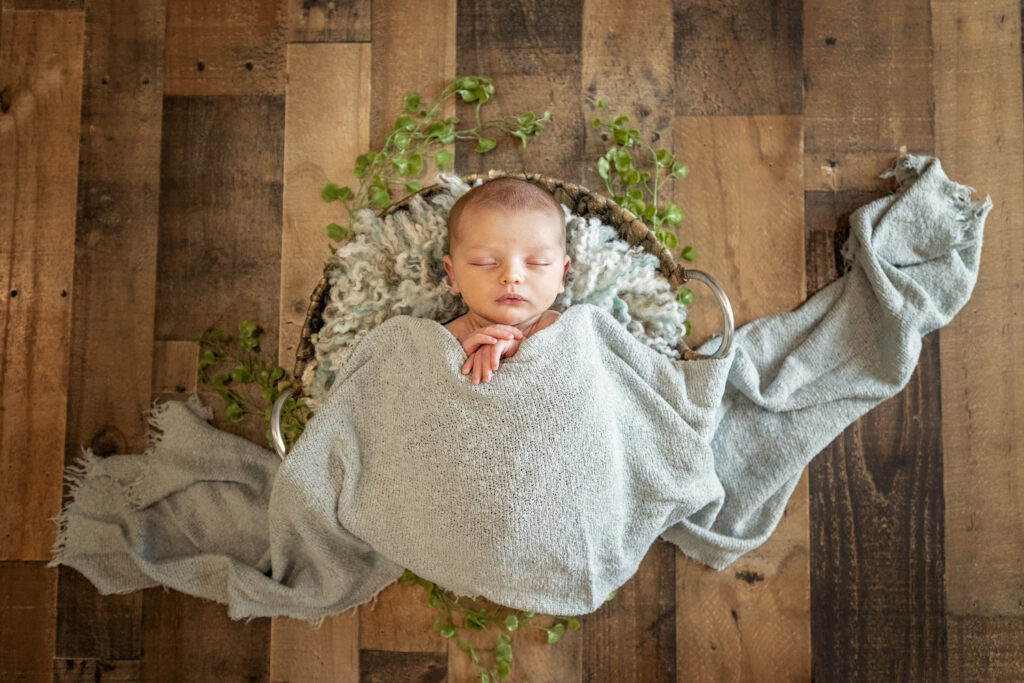 newborn boy in a light blue wrap laying in a round basket