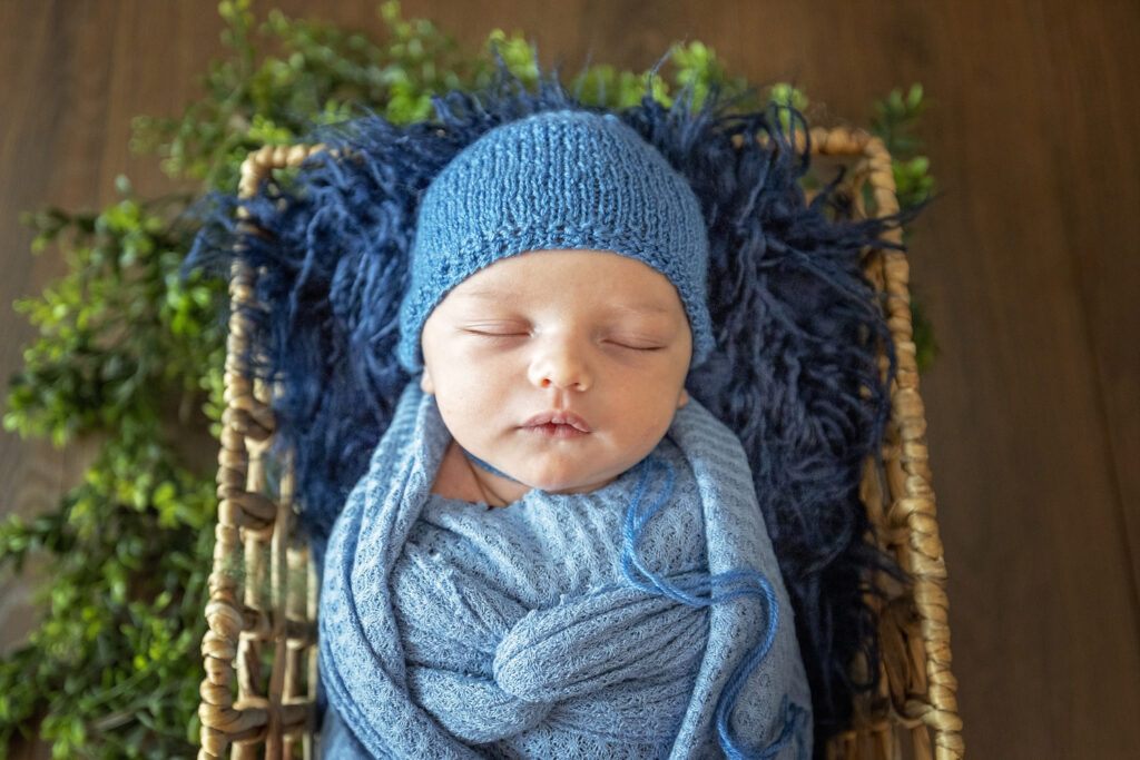 newborn boy in a blue wrap laying on a dark blue faux fur with a blue bonnet