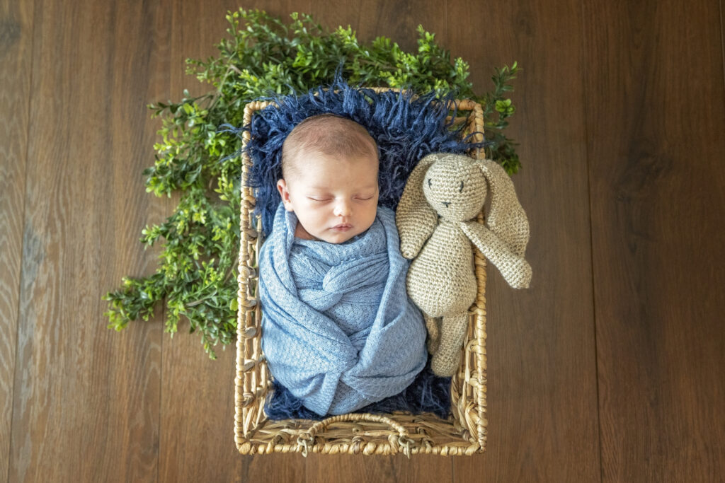 newborn boy in a blue wrap laying on a dark blue faux fur with a stuffed bunny