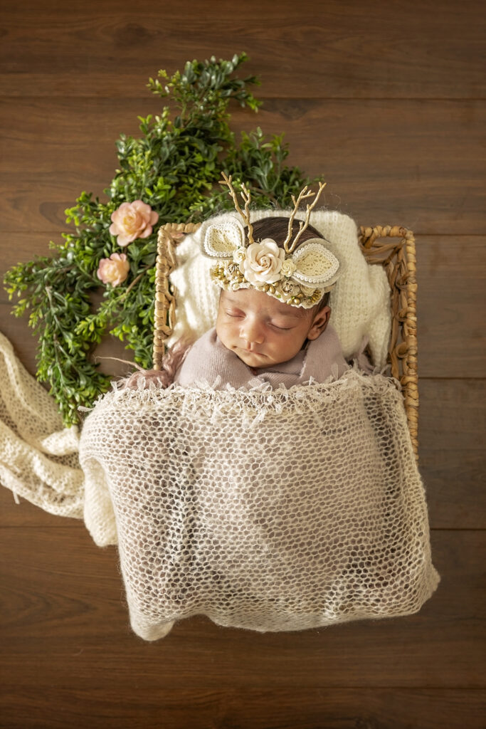 Newborn girl in a basket with a reindeer and flowers headband