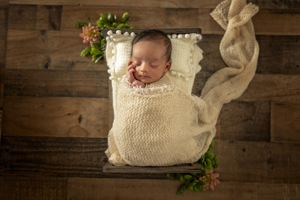 Newborn girl asleep on a small bed with a white wrap