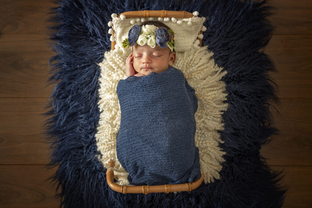 Newborn girl on a boho bed with a blue wrap and blue flower headband