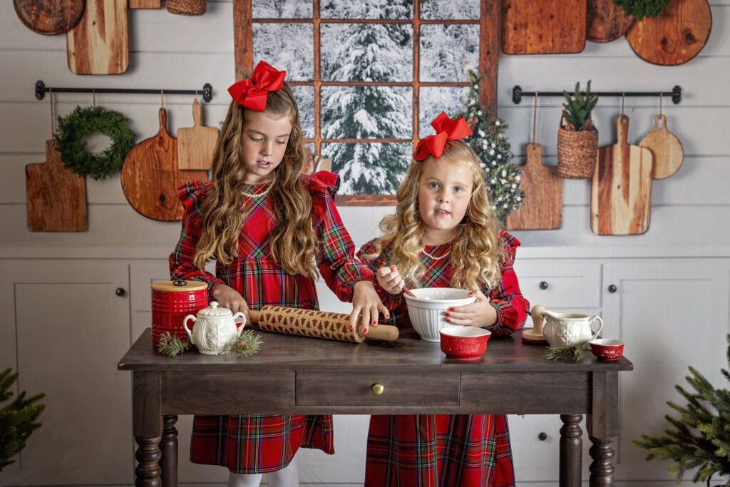 two young girls in red dresses baking together in a Christmas themed kitchen