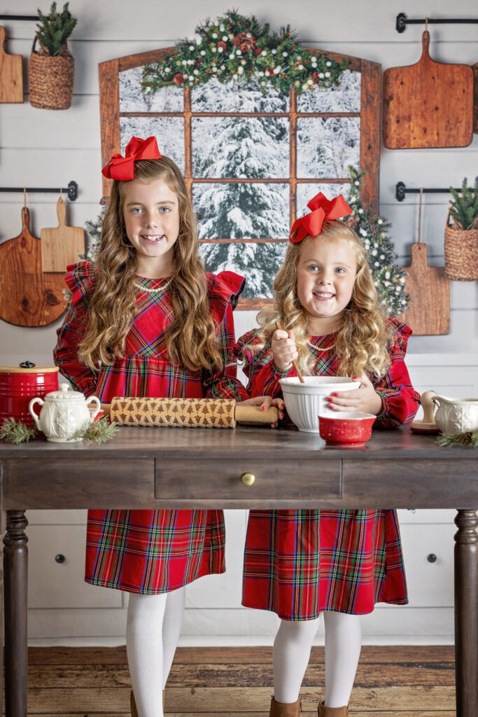 two young girls in red dresses baking together in a Christmas themed kitchen