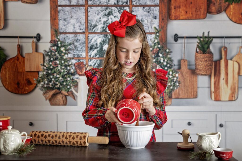 young girl in a red dress pouring ingredients in a mixing bowl while in a Christmas kitchen