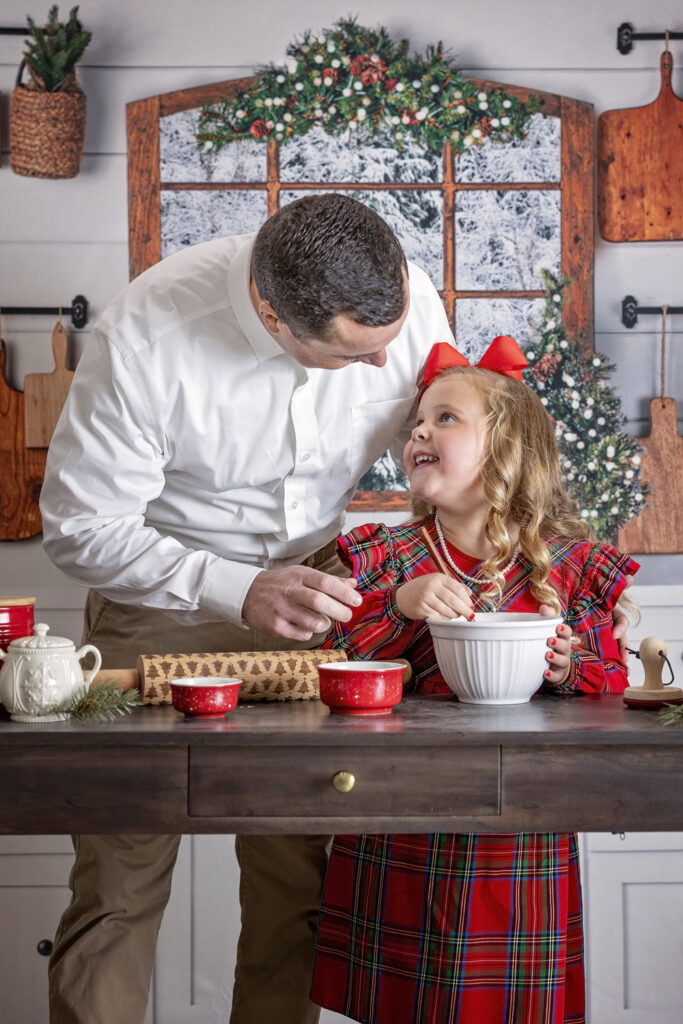 young girl in a red dress making cookies with her dad in a Christmas kitchen