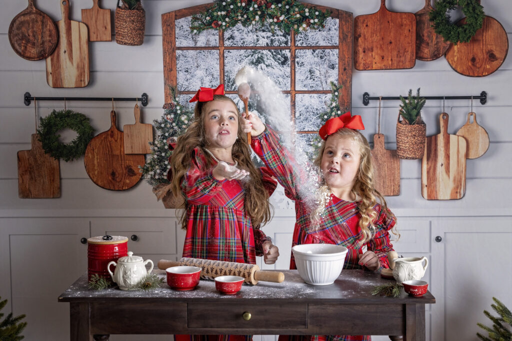 two young girls in red dresses throwing flour in a Christmas kitchen