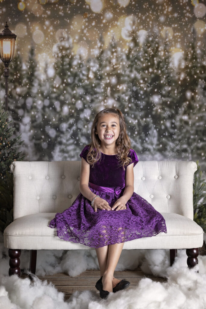 young girl in a purple dress sitting on a sofa in a Christmas tree farm