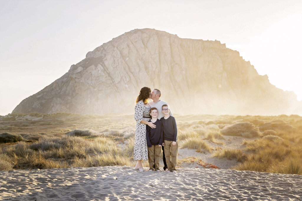 family of four at Morro Rock with mom and dad kissing