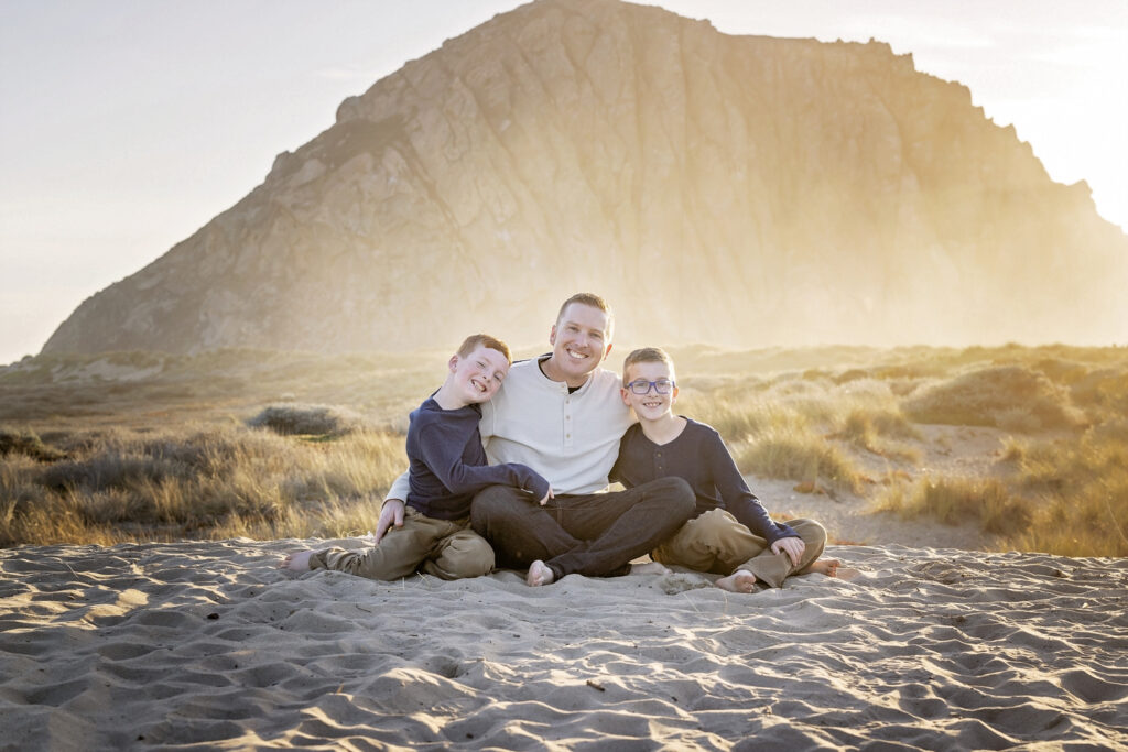 father sitting in the sand with his two sons at the beach