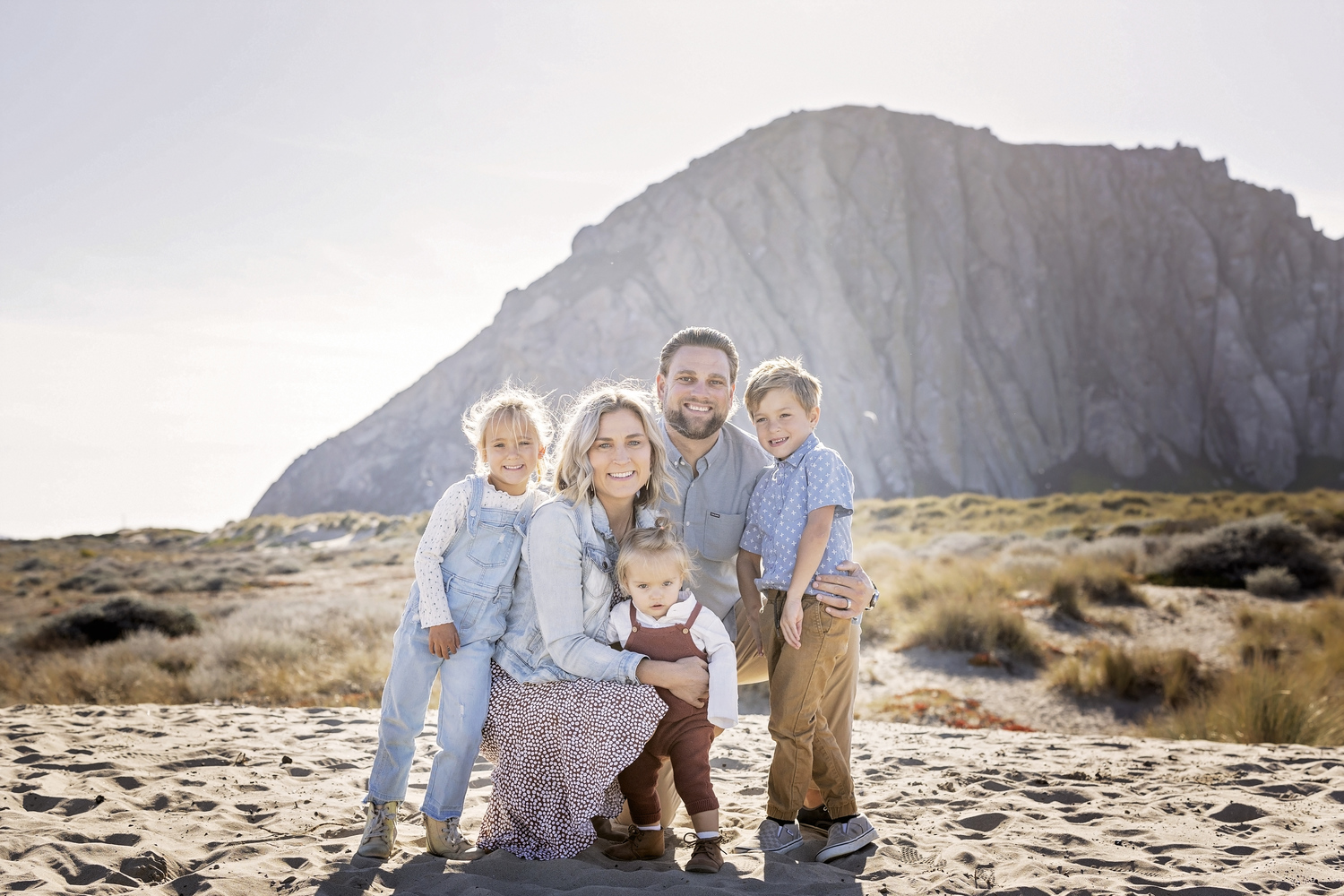 family of five posing together in the sand with Morro Rock behind them