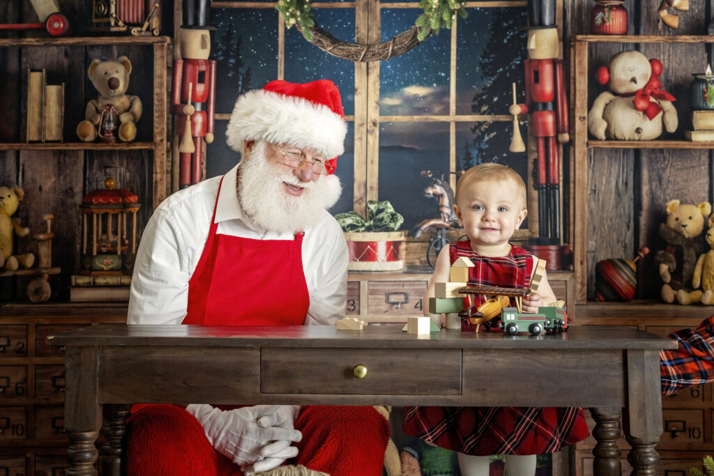 one year old girl stacking blocks with Santa Claus in his workshop