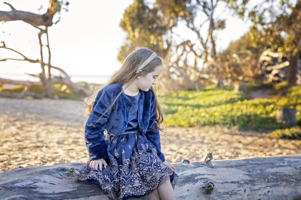 young girl in a blue dress looking down at a log