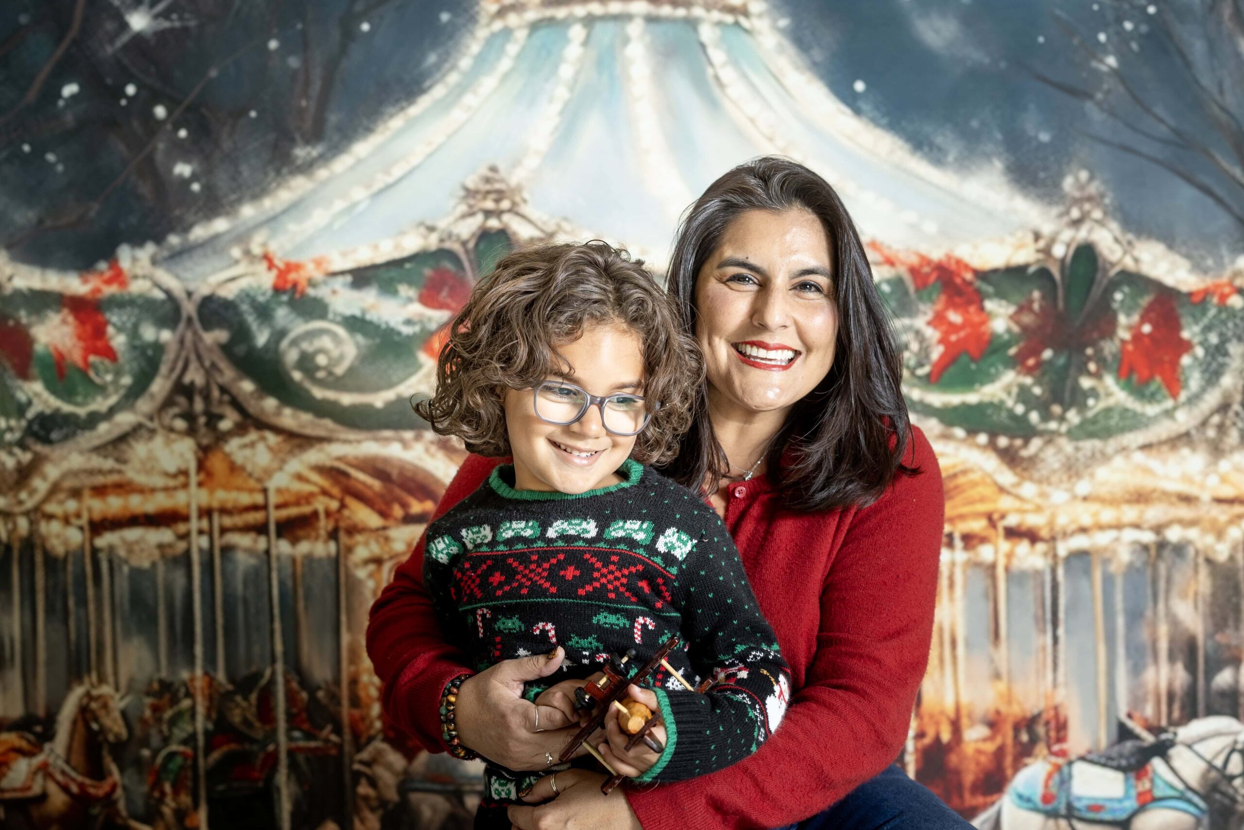 Mother and son sitting together in front of a Christmas carousel backdrop