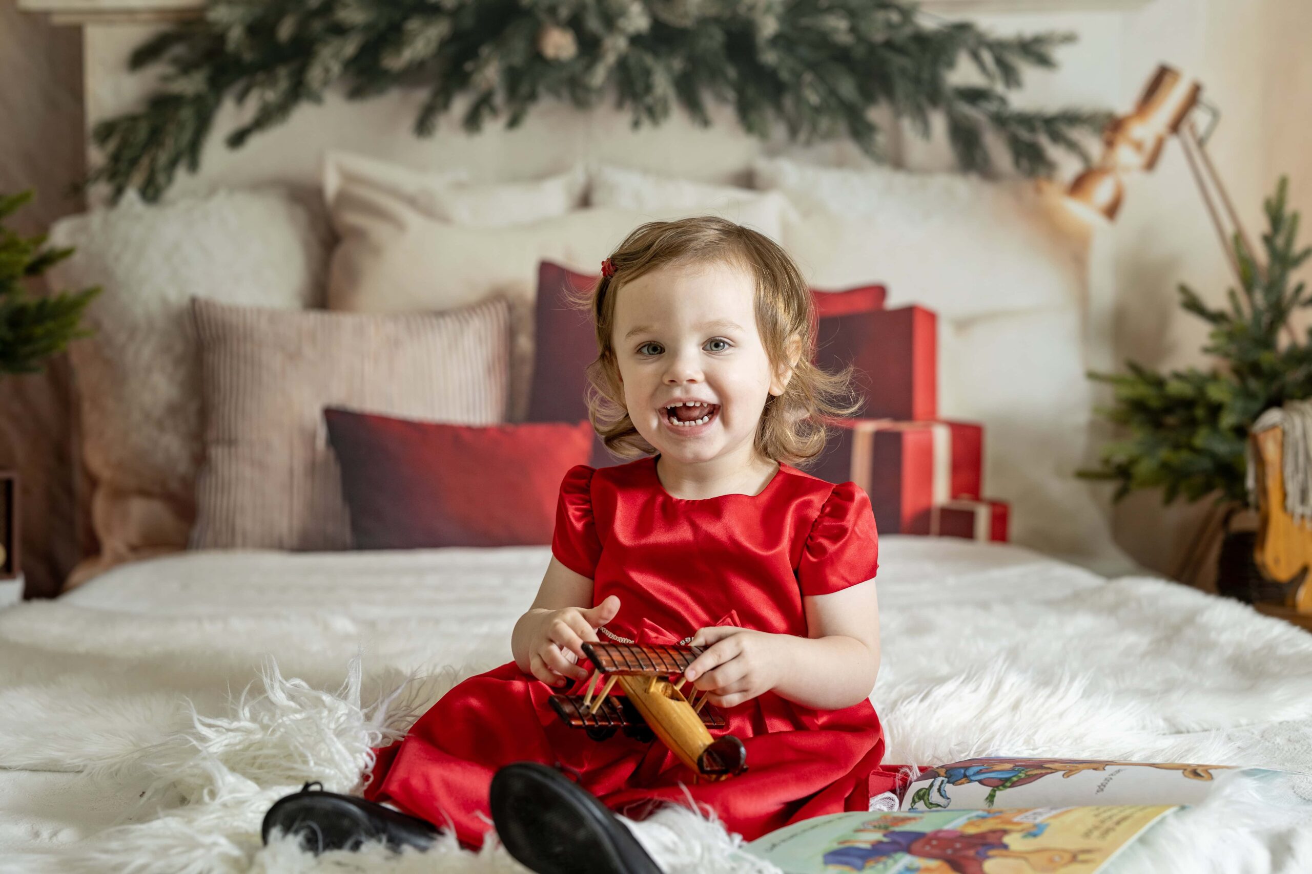 Young girl in a red dress sitting on a bed while playing with a wood toy airplane