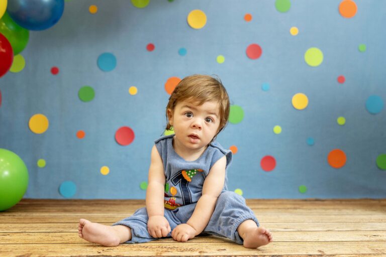 one year old boy in a blue outfit sitting on a wood floor with a blue polka-dotted background