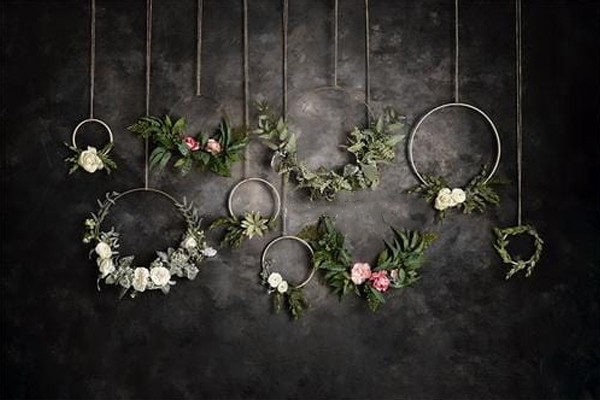 A collection of modern floral hoops in varying sizes, hanging against a dark textured backdrop. Each hoop is adorned with minimalist greenery and soft blooms in shades of white, blush, and pink, creating an elegant, boho-inspired wall display.