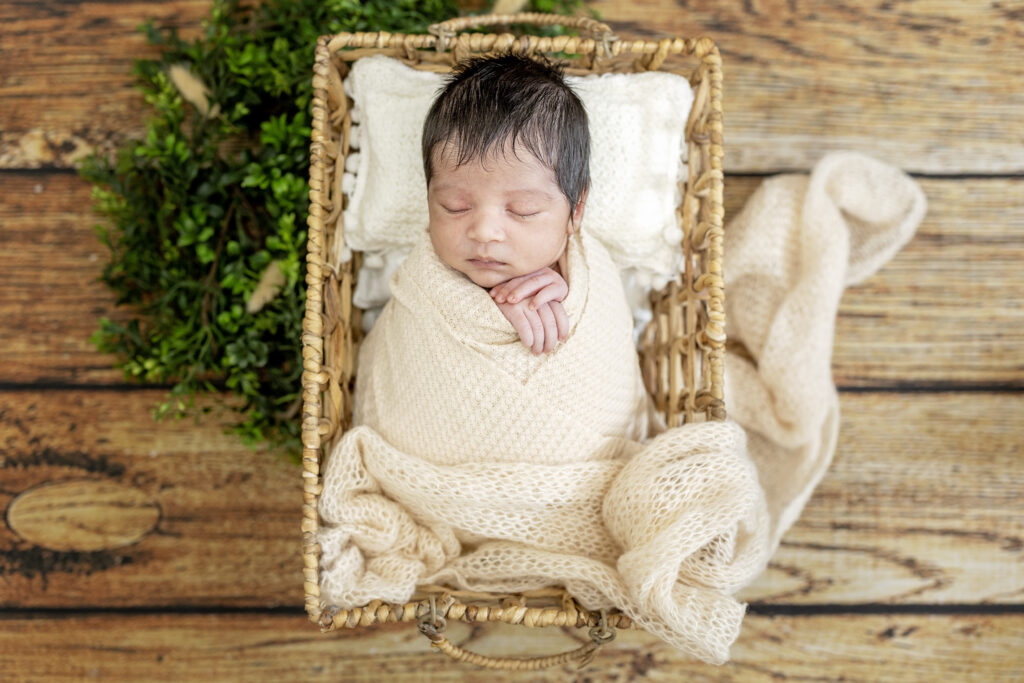 Newborn boy wrapped in a cream knit blanket, sleeping peacefully on a rustic wooden backdrop.