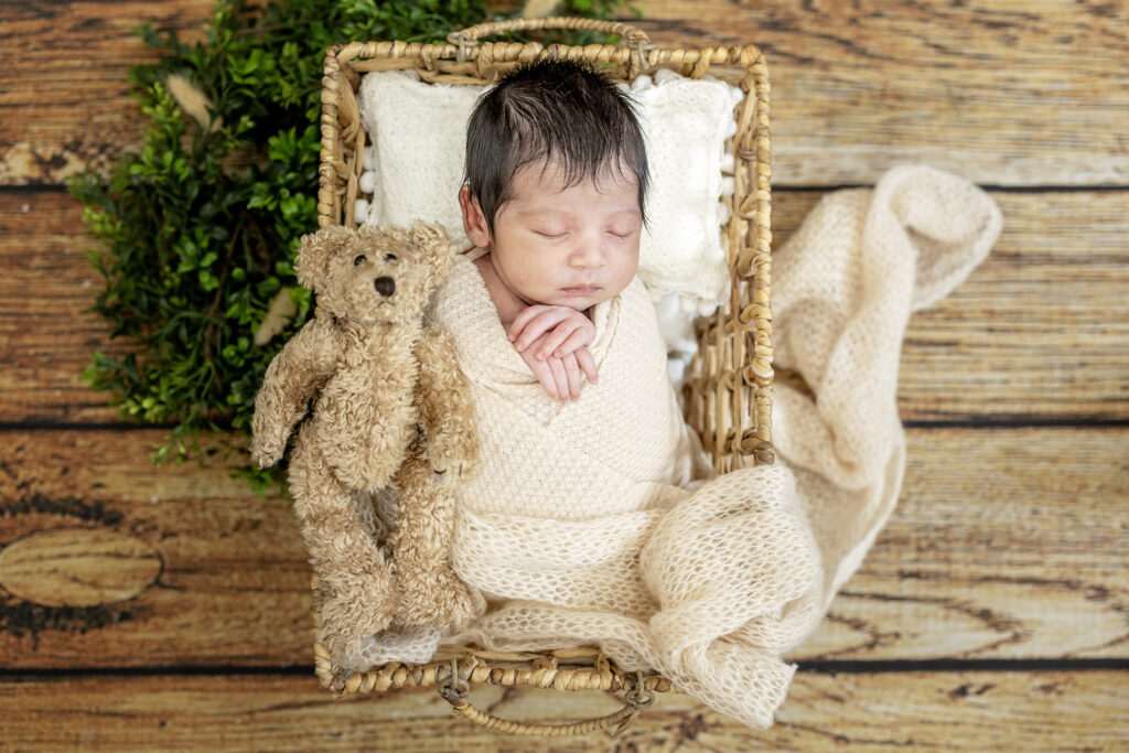 Baby in a soft neutral wrap resting on textured layers during a professional newborn session.