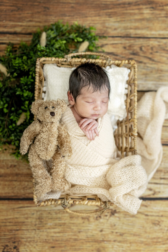 Overhead view of a newborn boy wrapped in cream fabric, surrounded by cozy textures.
