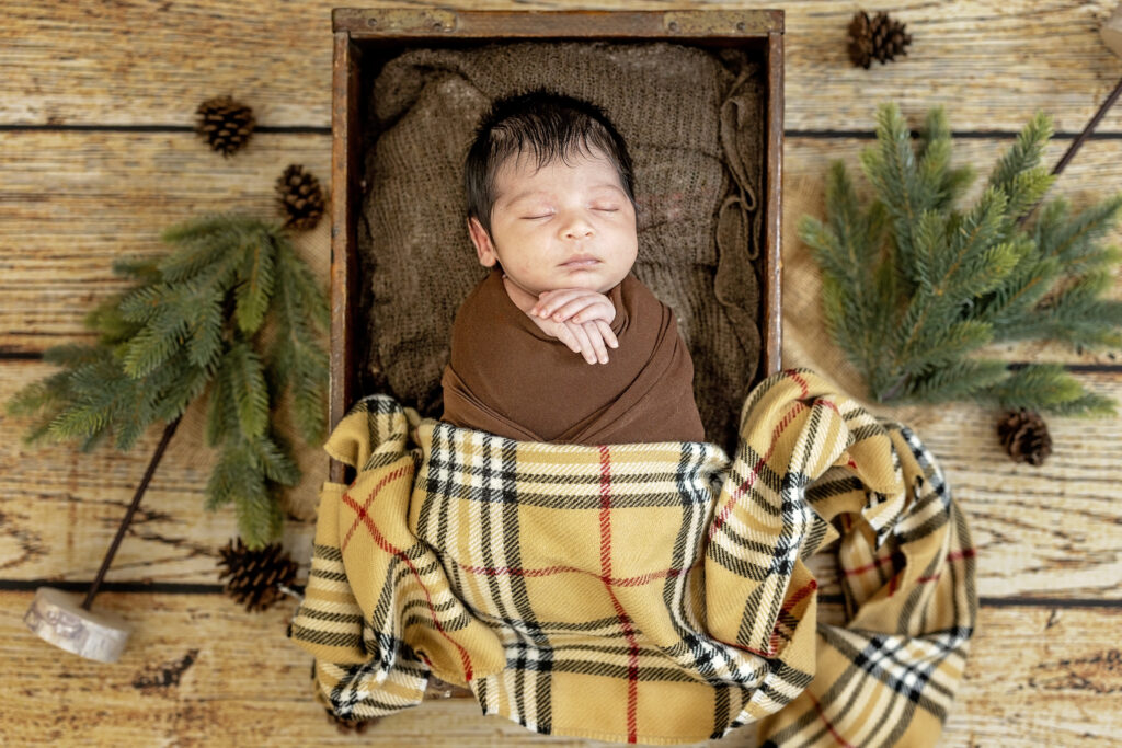 Cozy newborn boy swaddled in yellow plaid blanket, resting on soft fabric layers.