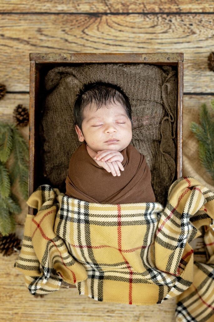 Sleeping baby wrapped in brown tones with wooden backdrop, rustic newborn photography setup.