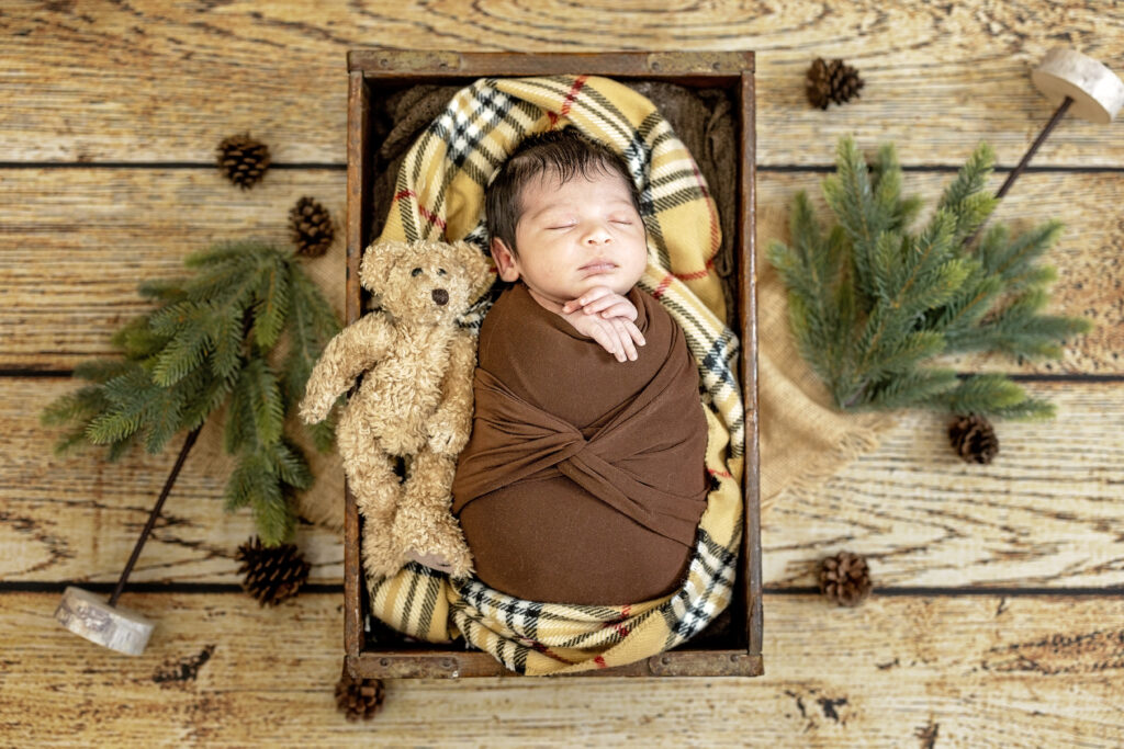 Baby boy sleeping peacefully in a rustic wooden bowl surrounded by neutral textures.