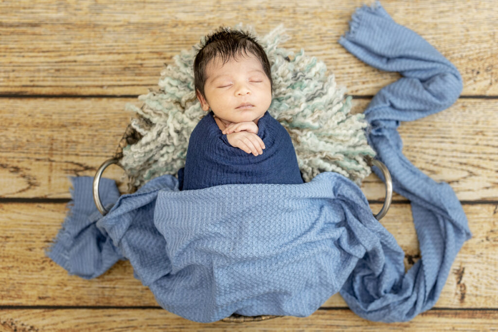 Baby boy wrapped in denim-blue fabric, sleeping soundly on a rustic backdrop.