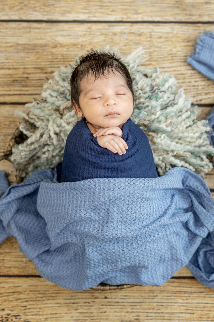 Cozy newborn wrapped in blue blanket, posed on faux fur for studio session.