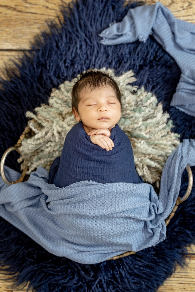 Wrapped newborn boy with fuzzy blue textures, classic baby photography pose.