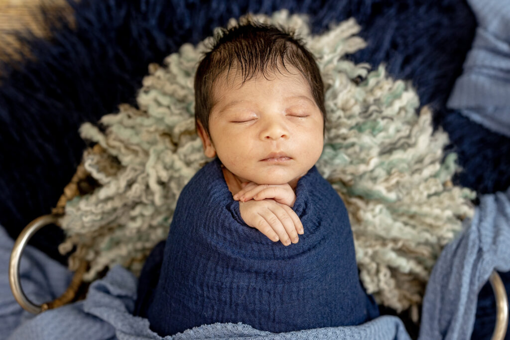 Close-up of baby’s face swaddled in blue tones, natural light highlighting features.