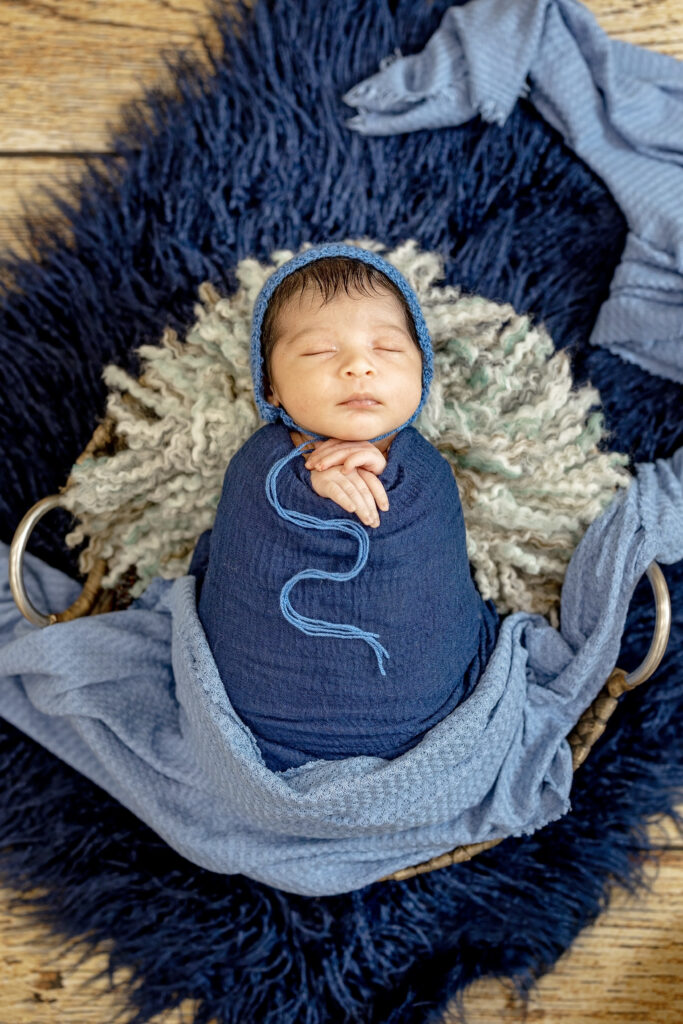 Newborn baby peacefully asleep in round basket with navy and cream textures.