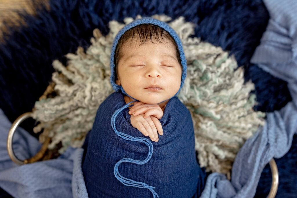 Baby boy in cozy blue wrap, photographed against faux fur for a dreamy studio portrait.